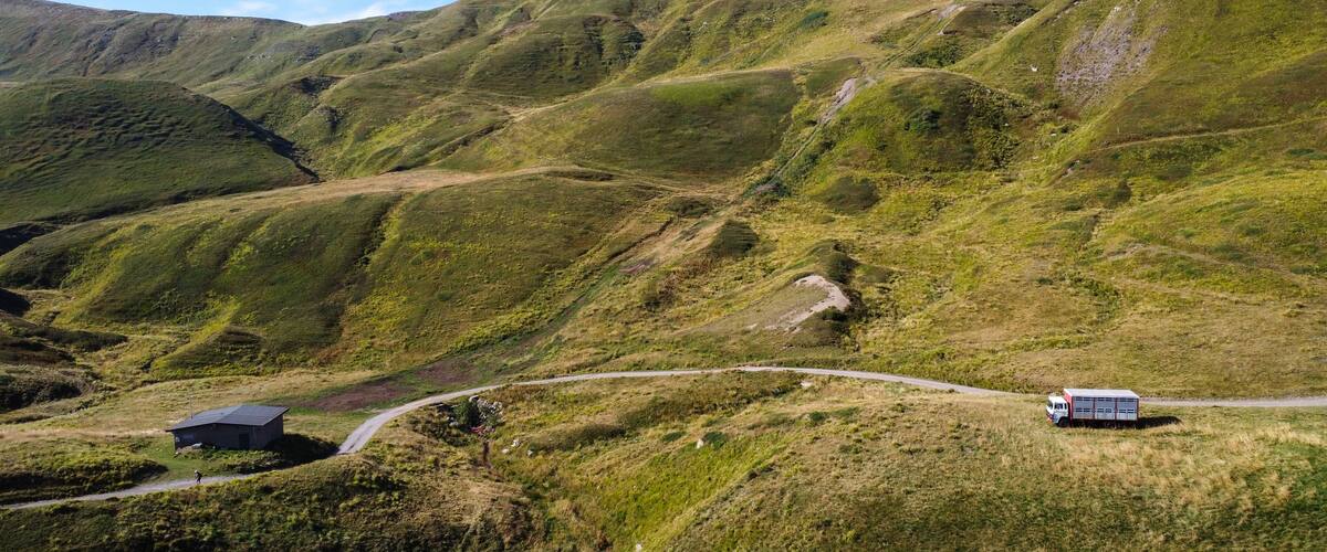 A winding road through a mountainous landscape with grassy slopes and a small building on the left.