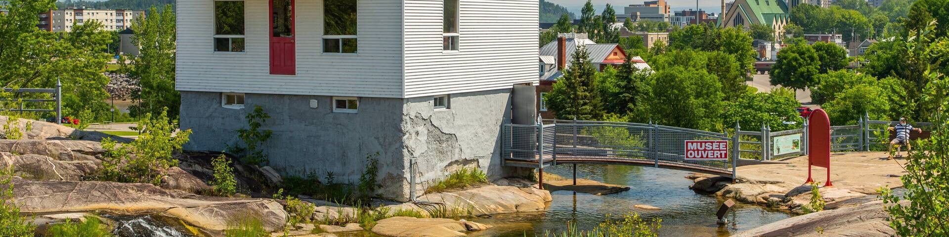 A white house with a red door, a small bridge, and a museum sign.