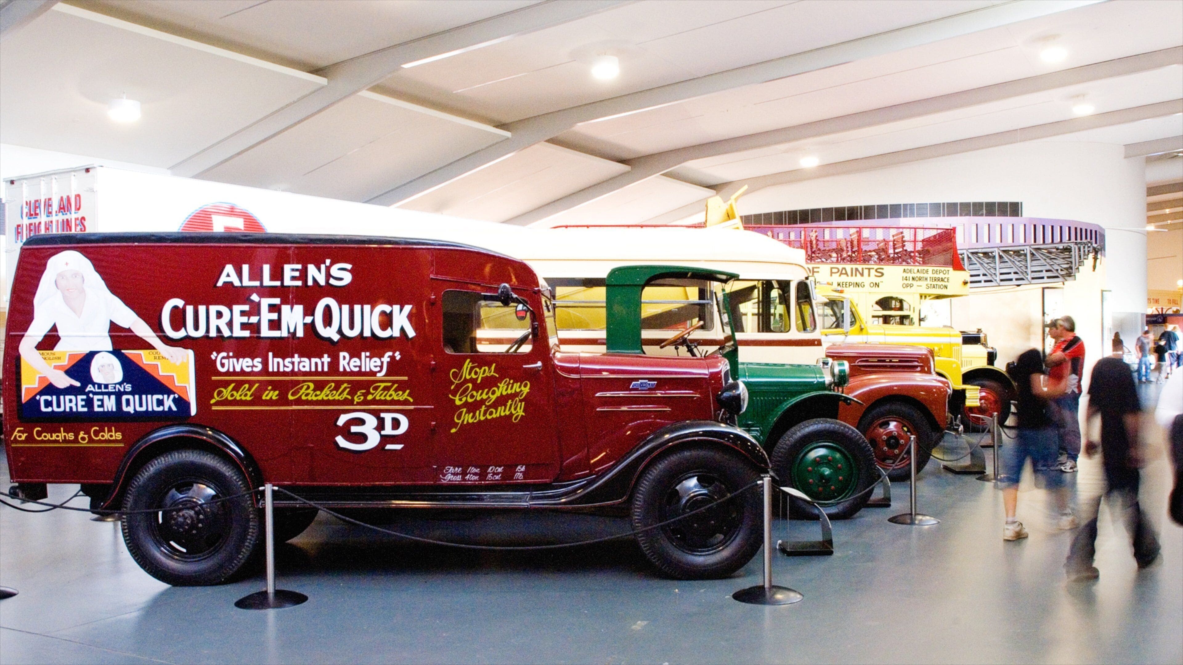 Vintage trucks on display, including a red truck labeled 'ALLEN'S CURE-EM-QUICK'.