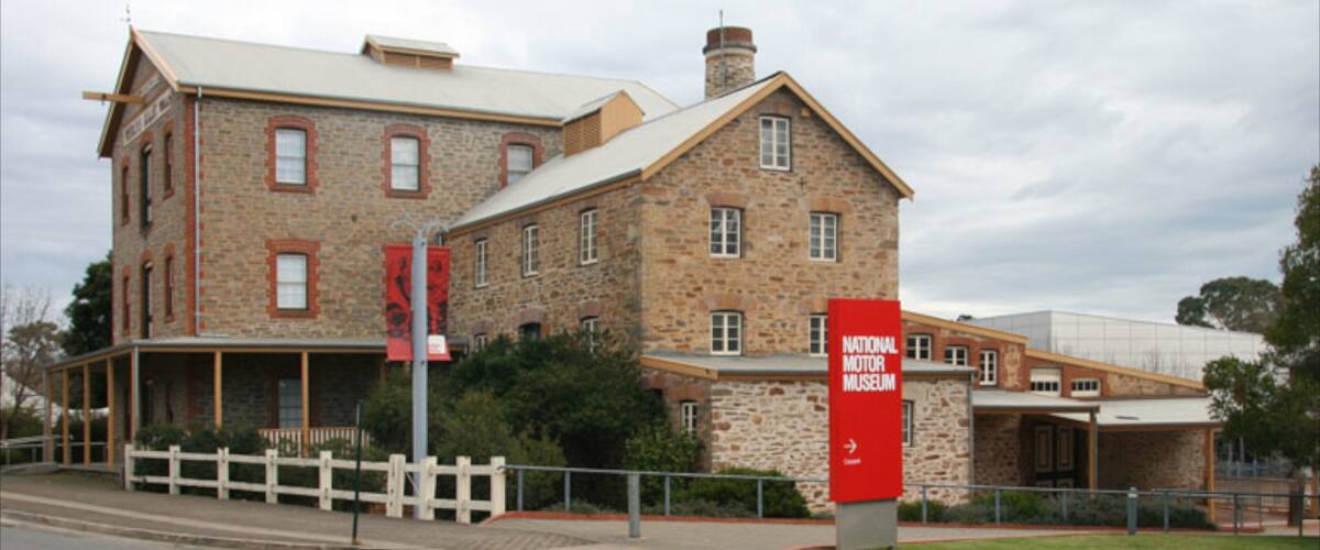 A historic stone building with a red banner for the National Motor Museum.