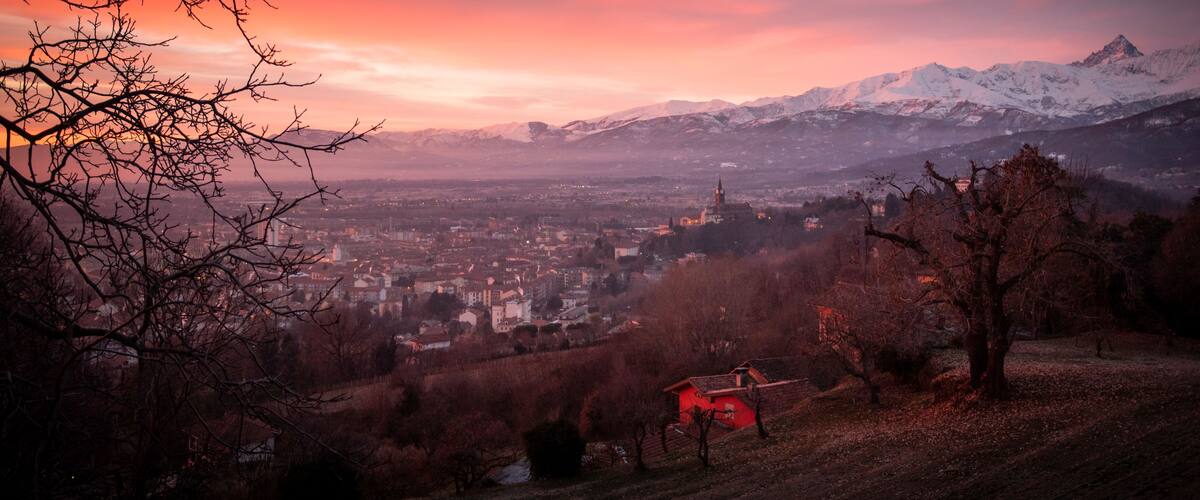 Un paisaje montañoso con una ciudad en el valle, una torre de iglesia destacada y una casa roja en una colina.