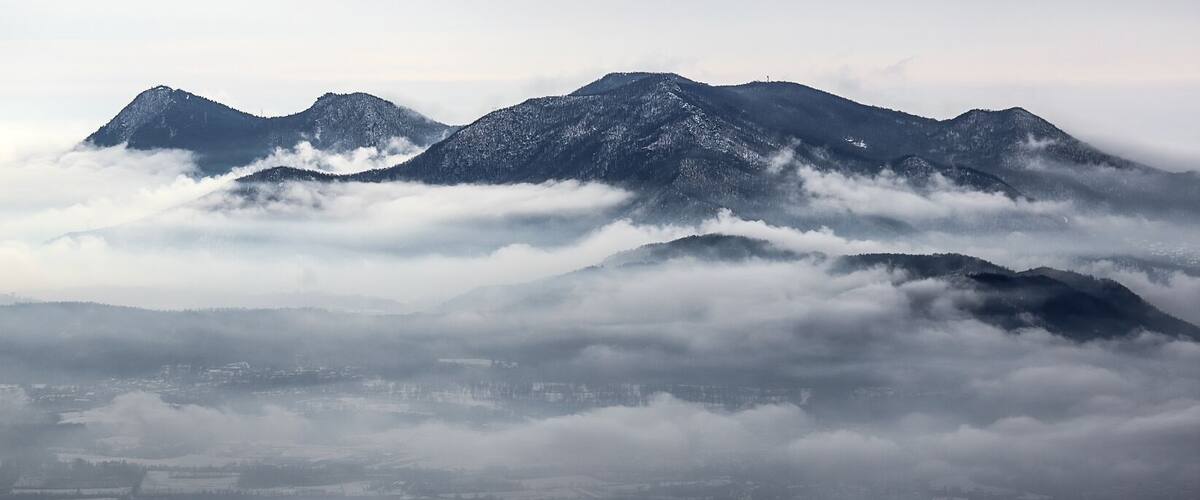 Paisatge de muntanyes amb cims nevats i una vall propera amagada en boira.