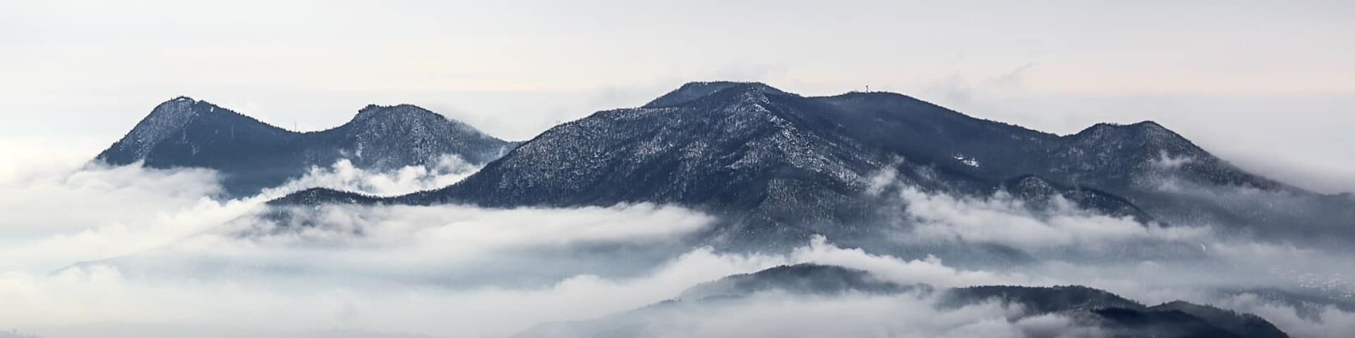 A mountainous landscape with snow-covered peaks and a valley below shrouded in clouds.