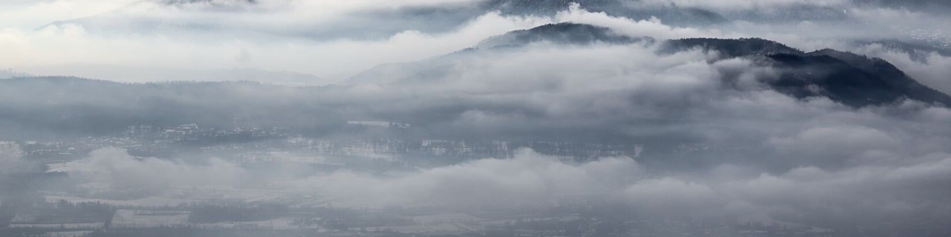 Un paisaje montañoso con picos nevados y un valle en la falda cubierto de nubes.