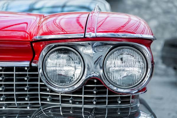 Many classic red vintage old american cars parked in row at garage, exhibition of fest. Close-up detail view beautiful retro oldtimer vehicle hood, headlight, fender and shine chrome plated bumper