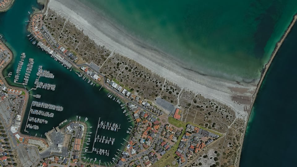 An aerial view of a coastal town with a marina, residential areas, and a beach.