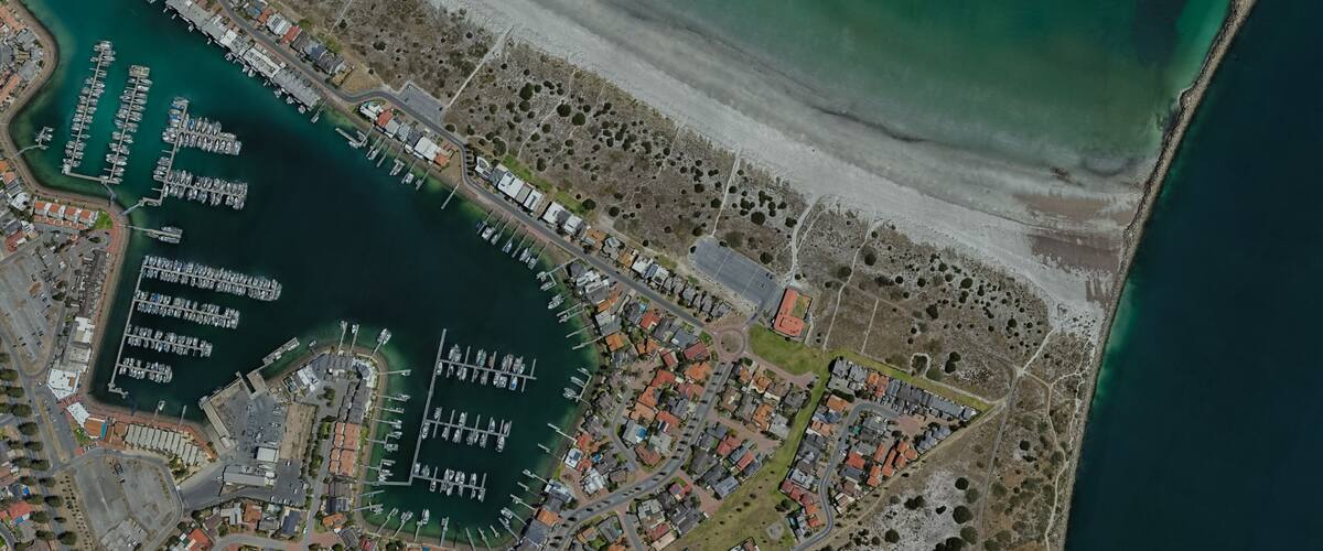 An aerial view of a coastal town with a marina, residential areas, and a beach.