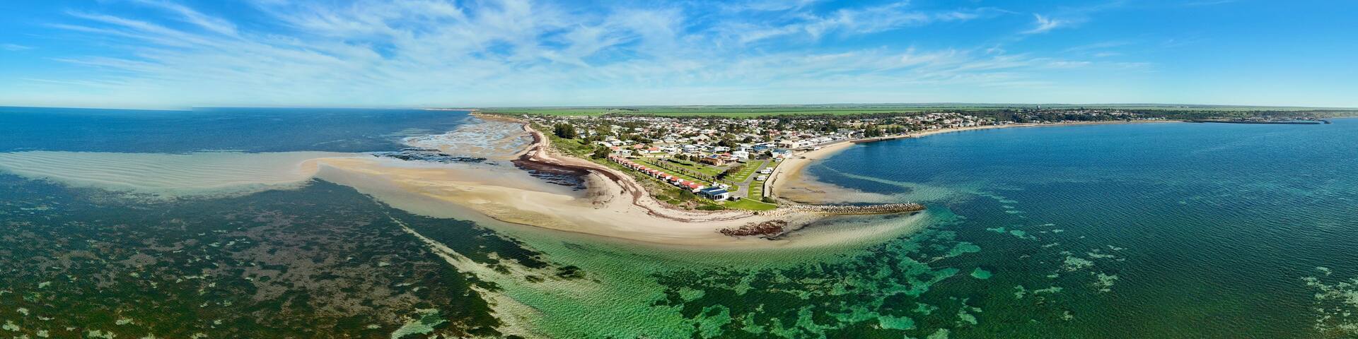 A coastal town with a beach, clear blue waters, and a distant shoreline.