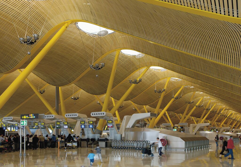 Terminal de aeropuerto con vigas estructurales amarillas y múltiples mostradores de facturación.