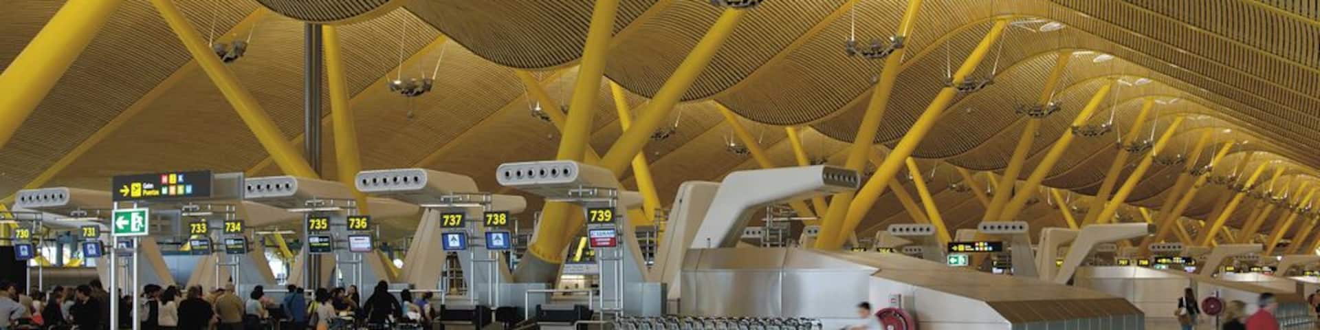 An airport terminal with yellow structural beams and multiple check-in counters.