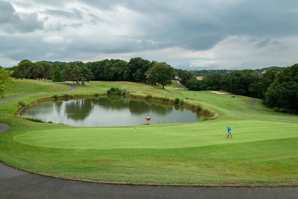 Ein Golfplatz mit Teich, Bäumen und bewölktem Himmel.