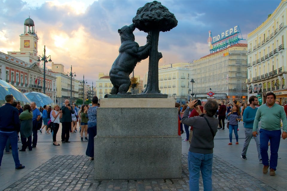 A statue of a bear climbing a tree in a public square with people around.
