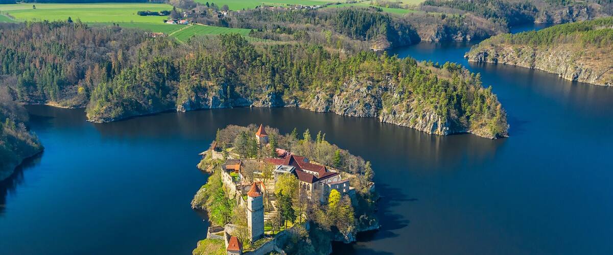 An island with a castle surrounded by a river and forested hills.