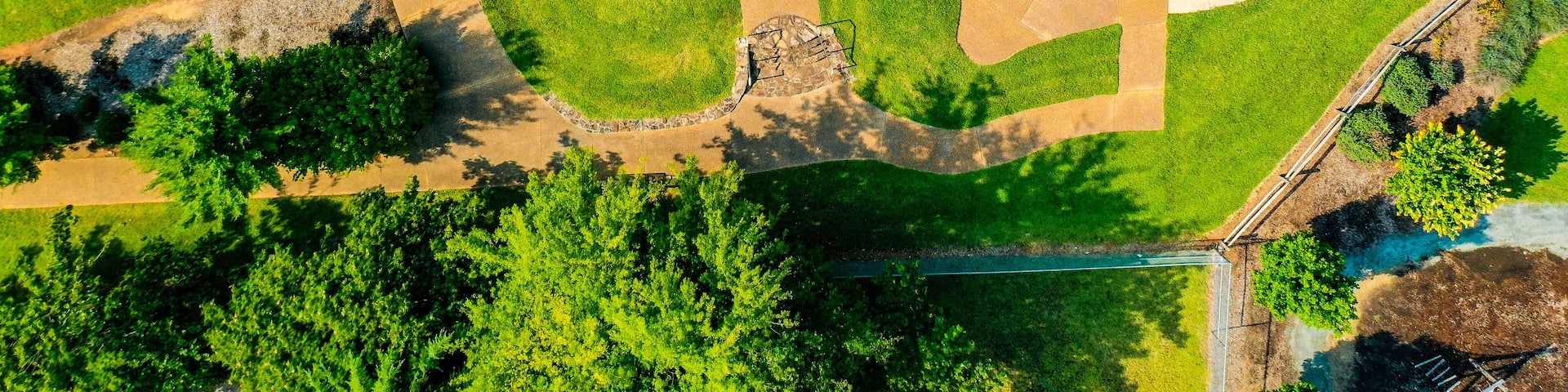 An aerial view of a park with a winding path, a central grassy area, and a bridge.