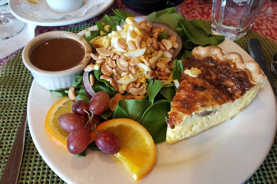 Um prato com uma fatia de quiche, uma salada com nozes e uvas, e uma tigela de molho.