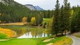 Een rustige golfbaan met een vijver, omgeven door dichte bossen en bergen.