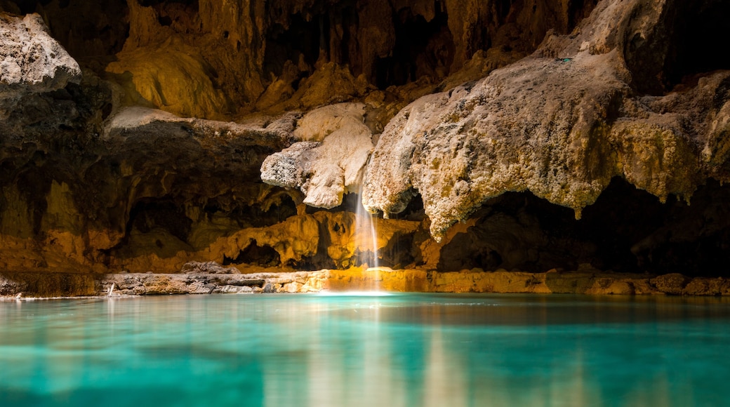 A small picturesque waterfall in a cave falls into a warm blue and green underground hot spring