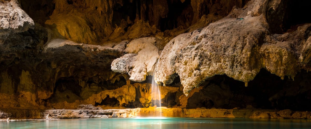 A small picturesque waterfall in a cave falls into a warm blue and green underground hot spring