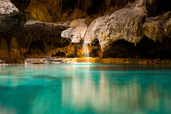 A small picturesque waterfall in a cave falls into a warm blue and green underground hot spring