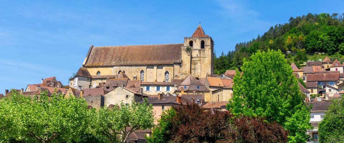 A historic church with a bell tower, surrounded by traditional buildings and lush greenery.