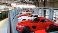 Eine Reihe roter Sportwagen, geparkt in einem Gebäude mit Metallgitter und einer Ziegelwand im Hintergrund.
