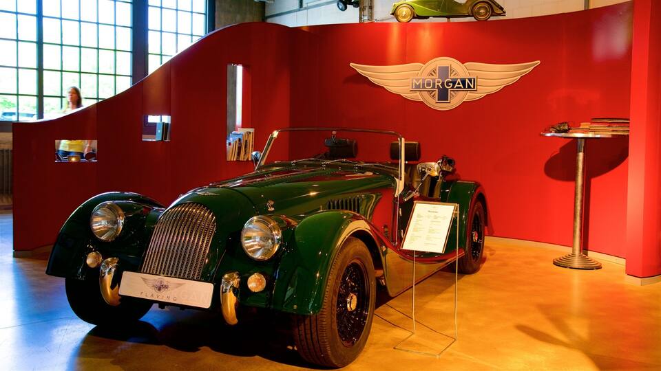 Un coche Morgan clásico exhibido en un museo, con una pared roja y un gran logotipo de Morgan.