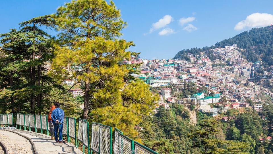A person standing on a bridge overlooking a densely populated hillside town with colorful buildings.