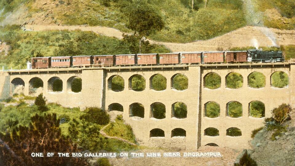 A train on a bridge with multiple arches, surrounded by greenery and hills.