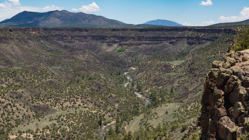 A canyon with a river, rocky cliffs, and distant mountains.