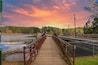 a metal and wooden rust colored bridge over a lake surrounded by lake water, green grass and lush green trees with powerful clouds and red sky at sunset at Murphey Candler Park in Atlanta Georgia USA
