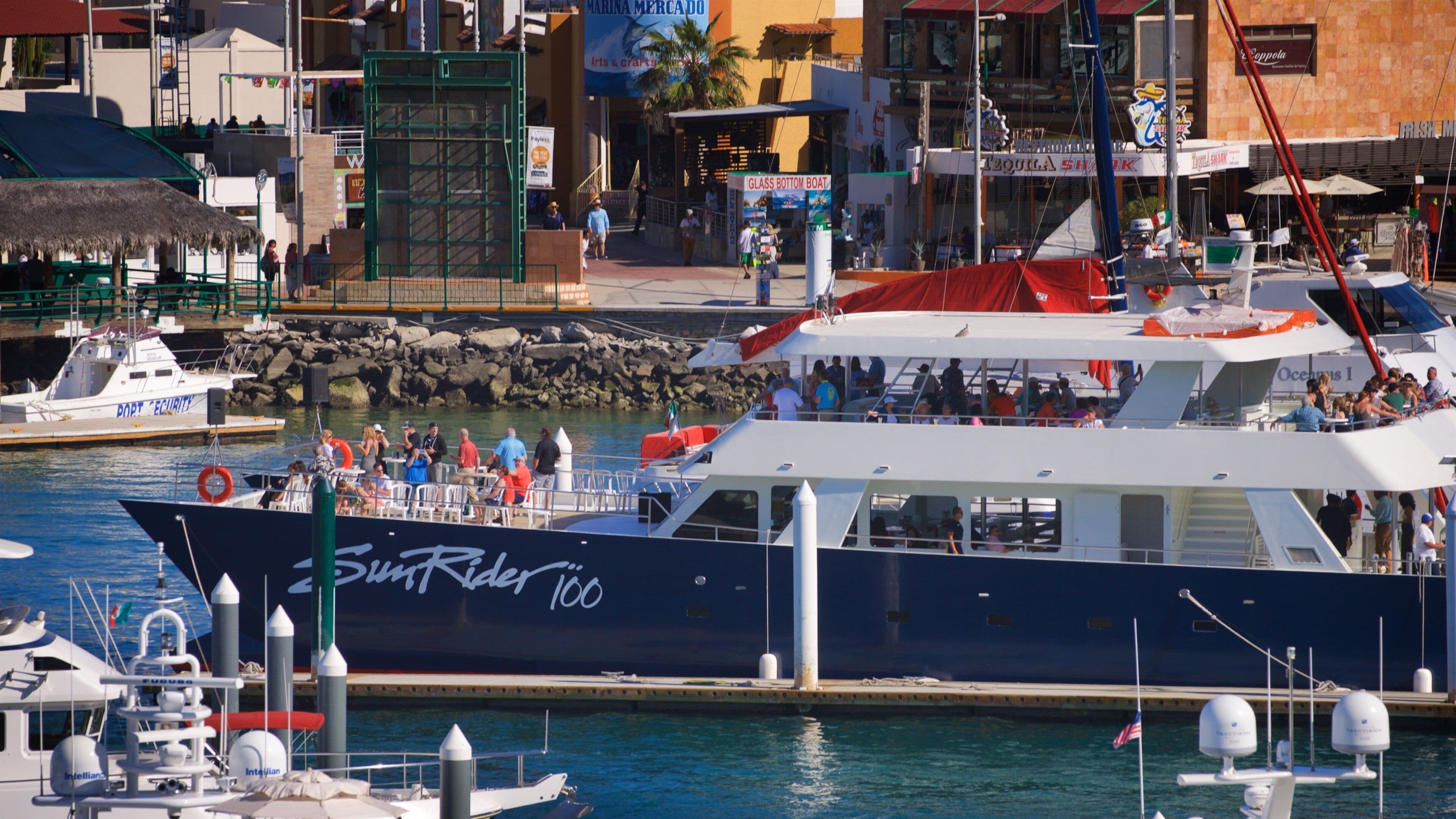 A large boat named 'SunRider 100' docked at a marina with a cityscape in the background.