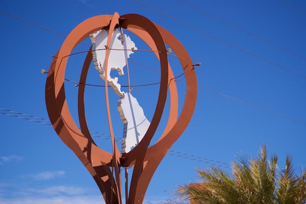 Une sculpture métallique représentant un globe, avec un cadre rouge, se détachant sur un ciel bleu clair.