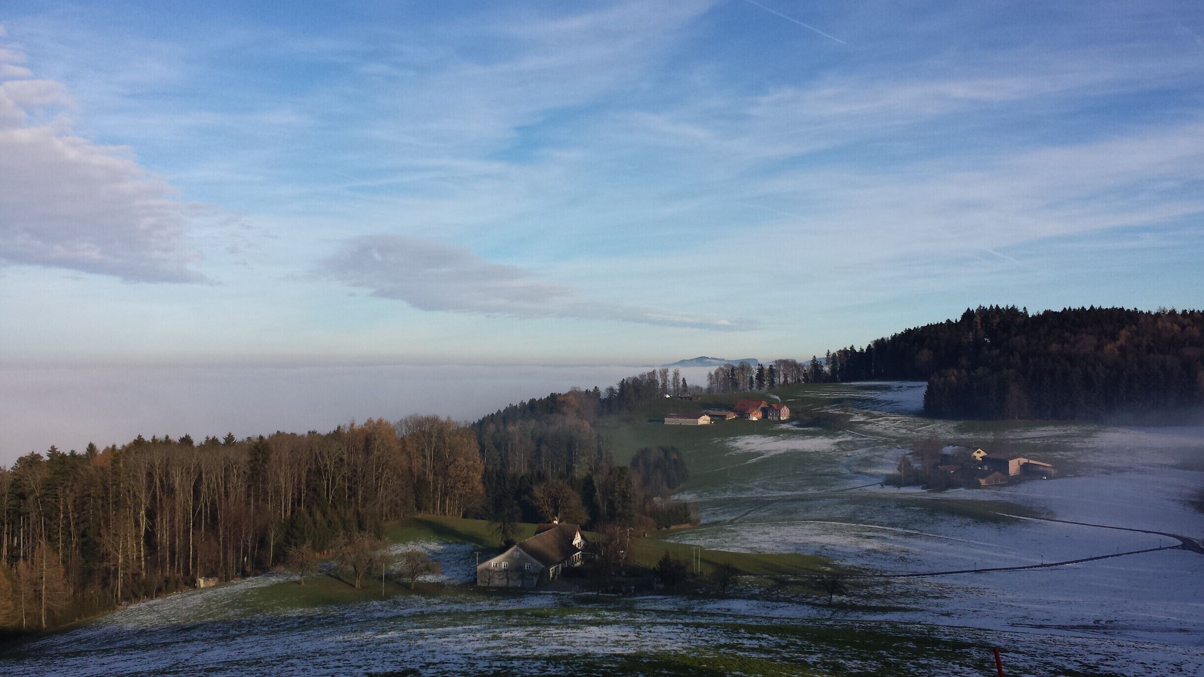 A rural landscape with a forested hill, scattered houses, and a clear sky.