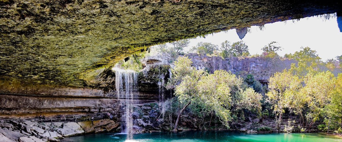 A turquoise pool with a waterfall under a cave.