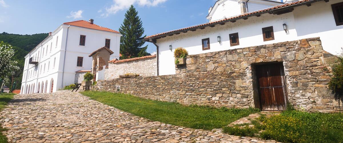 A cobblestone street leading to a white church with a bell tower and a stone wall.