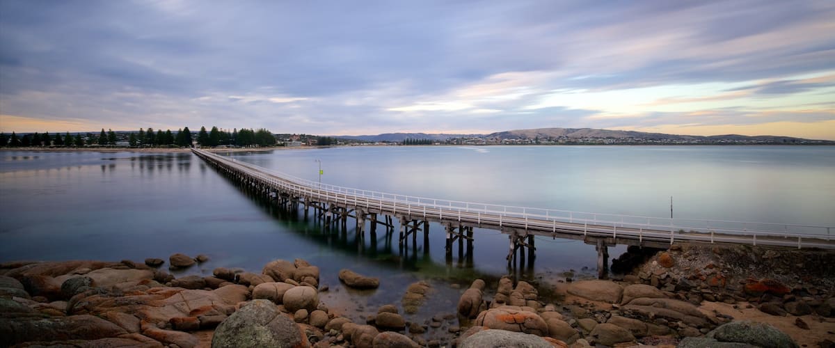 A calm lake with a long pier extending into the water, surrounded by rocks and trees.