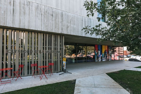 A modern building with a glass facade, red folding chairs, and a tree in the foreground.