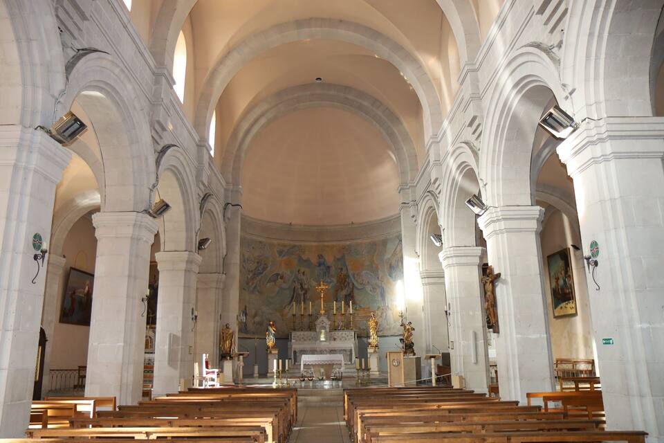 Interior de uma igreja com tetos em arco, bancos de madeira e estátuas religiosas.