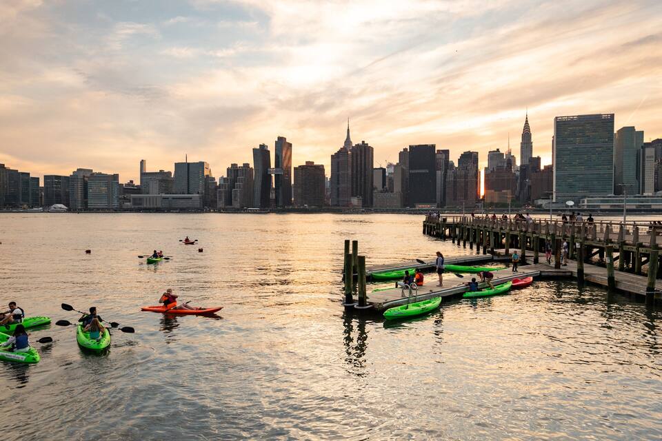 Ein Sonnenuntergang über der Skyline einer Stadt, während Kajakfahrer auf einem Fluss fahren.