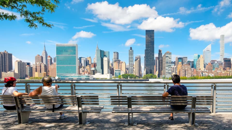 A waterfront park with benches overlooking a city skyline.