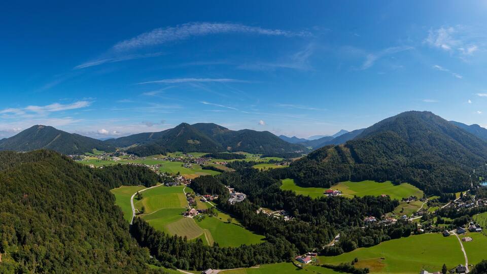A mountainous landscape with a lake, green fields, and scattered houses.