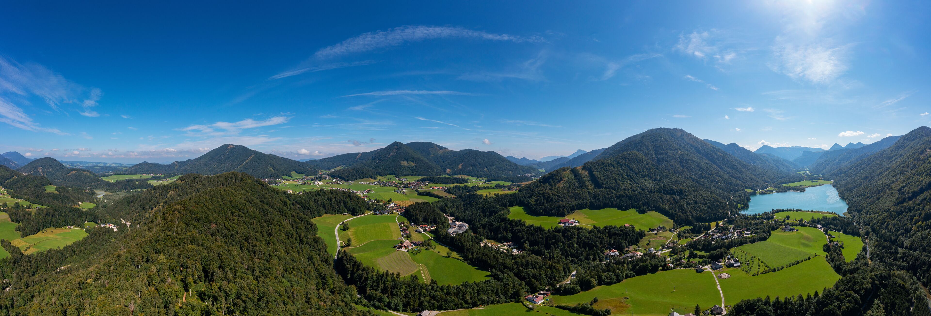 A mountainous landscape with a lake, green fields, and scattered houses.