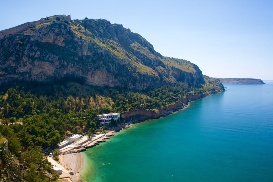 Un paysage côtier avec une grande montagne, une plage et un bâtiment situé près du rivage.