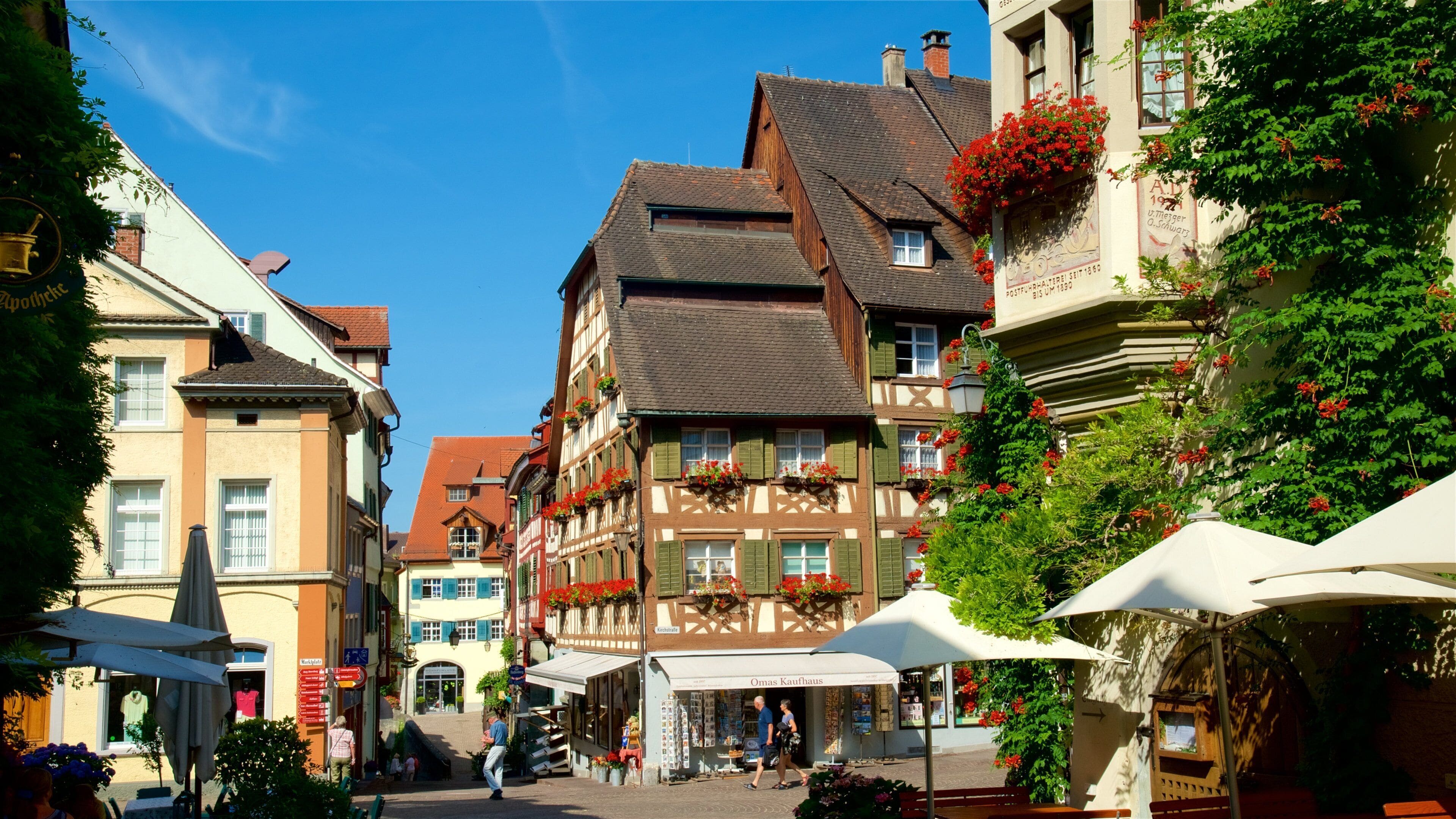 Une rue européenne bordée de maisons traditionnelles à colombages, de cafés en plein air et fréquentée par des piétons.