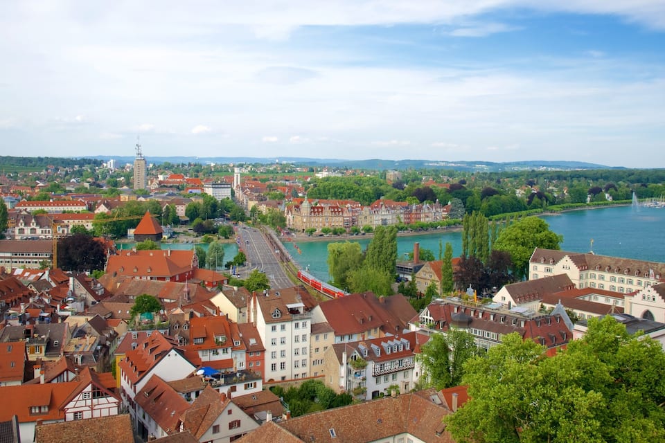 A riverside town with historic buildings, a bridge, and a distant tower.