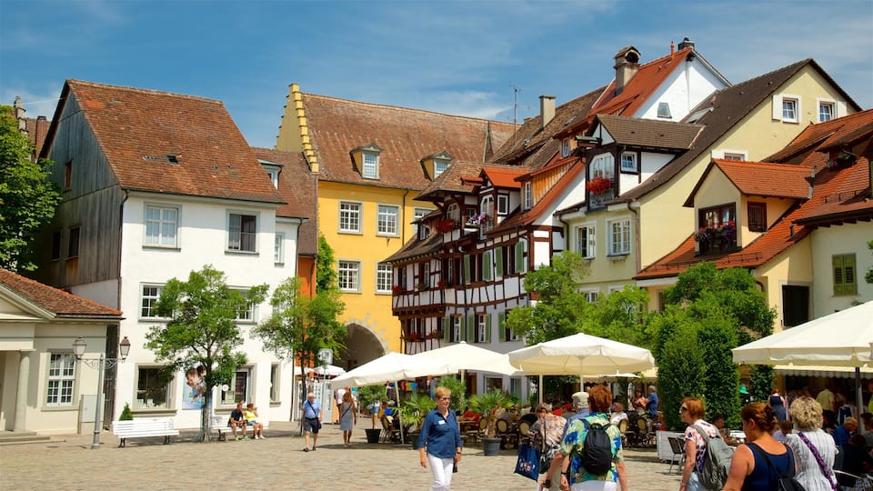 A cobblestone square with historic buildings, outdoor seating, and people walking.
