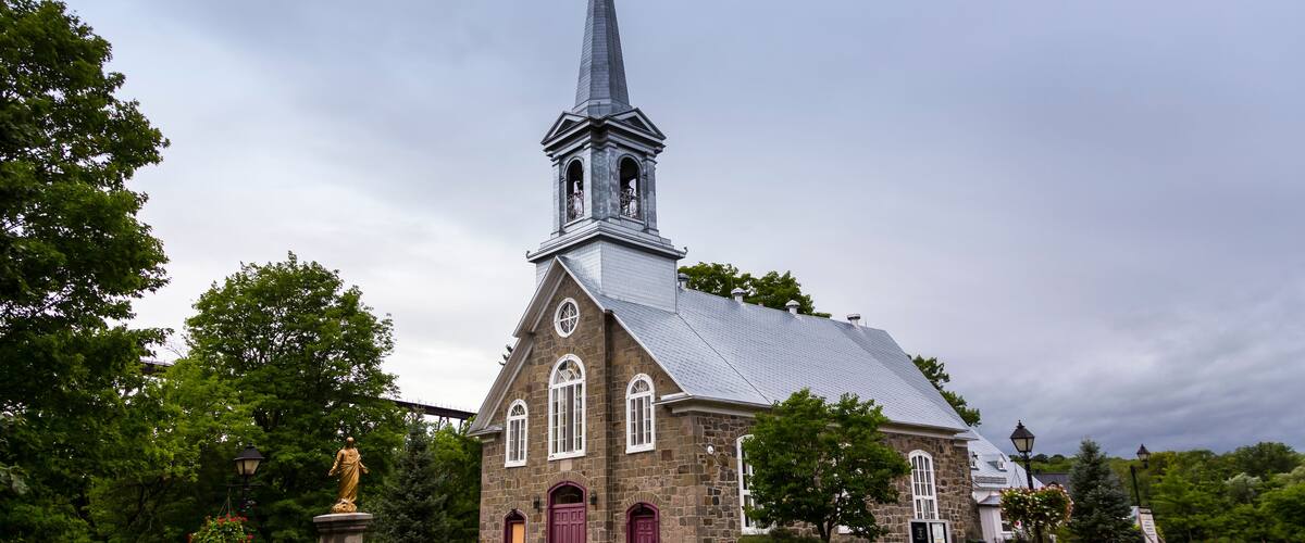 A church with a tall steeple, stone walls, and a statue in front.