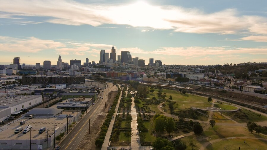 an aerial shot of the skyscrapers and office buildings in the city skyline over Los Angeles State Historic Park with lush green trees with blue sky and clouds at sunset in Los Angeles California