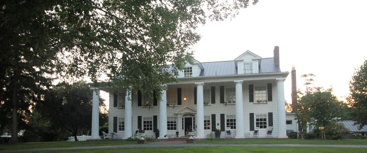 A large white colonial-style house with a front porch, columns, and a well-maintained lawn.