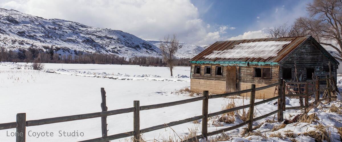 A snow-covered landscape with a rustic wooden cabin and a wooden fence.